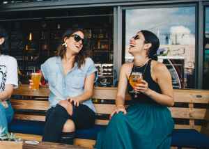 Two women, holding drinks and chatting happily